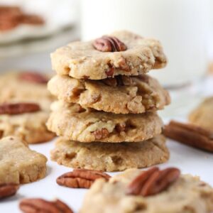 pecan sandies stacked on a white table with pecan halves scattered around.