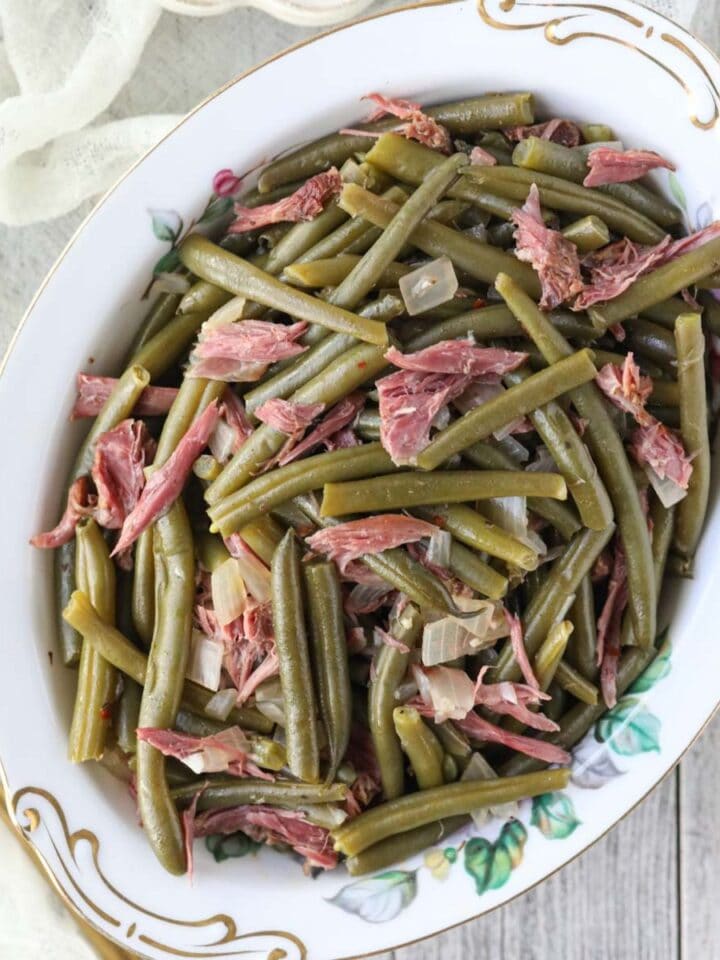 southern green beans in a white serving bowl on a white wood table.