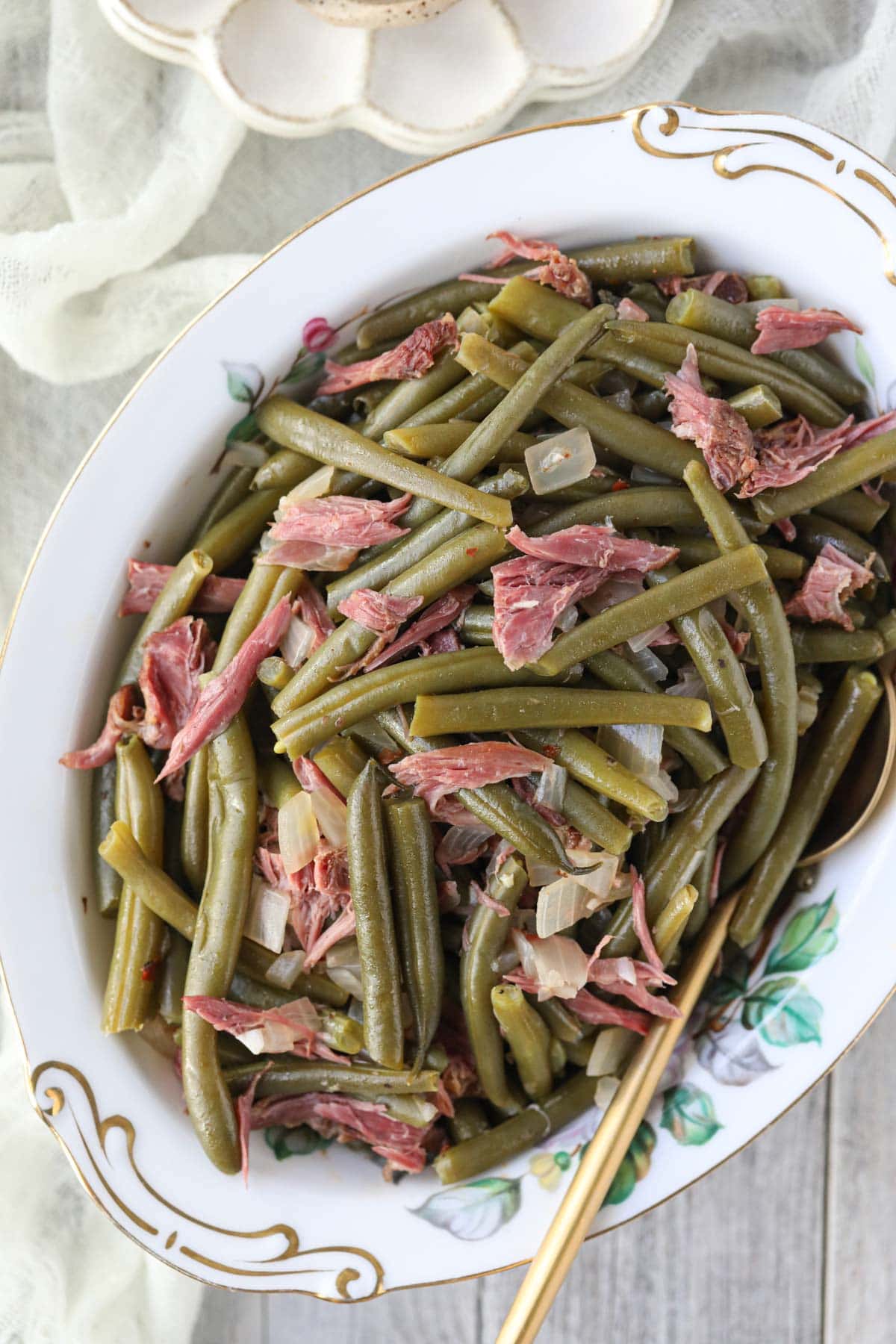 southern green beans in a white serving bowl on a white wood table.