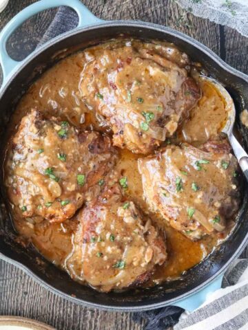 southern smothered chicken in a blue cast-iron skillet on a wooden surface.
