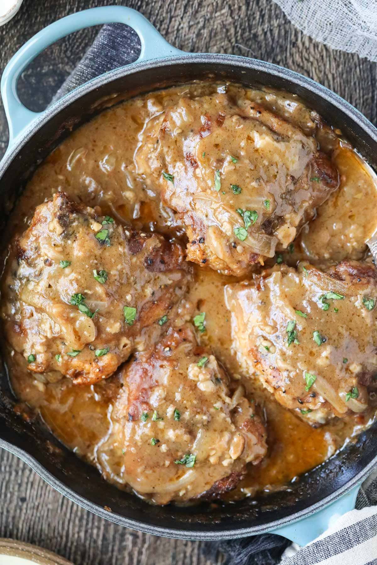 southern smothered chicken in a blue cast-iron skillet on a wooden surface.