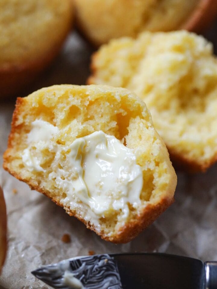 buttermilk cornbread muffin sliced open to show texture on parchment paper.