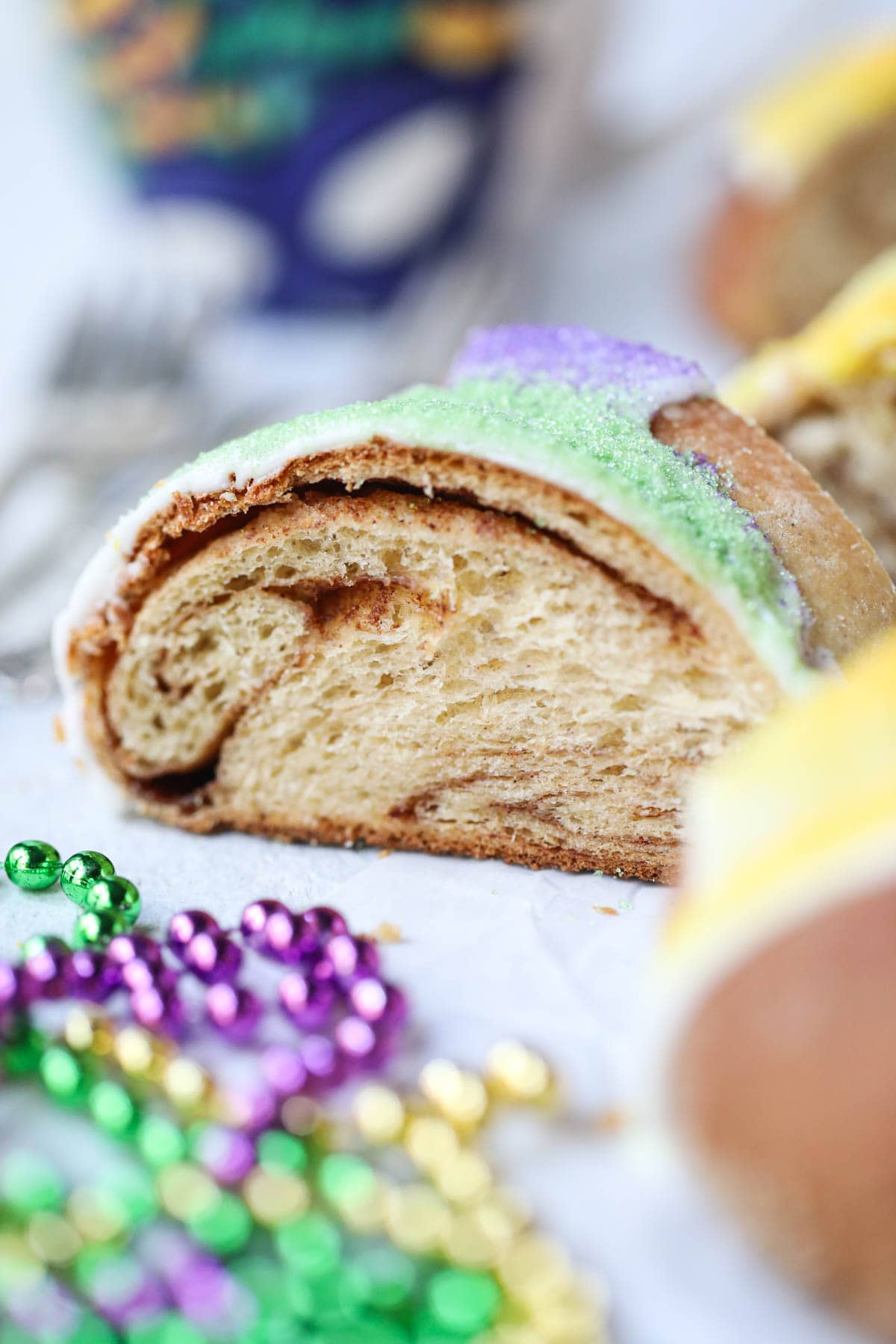 A slice of Mardi Gras king cake on a white surface.