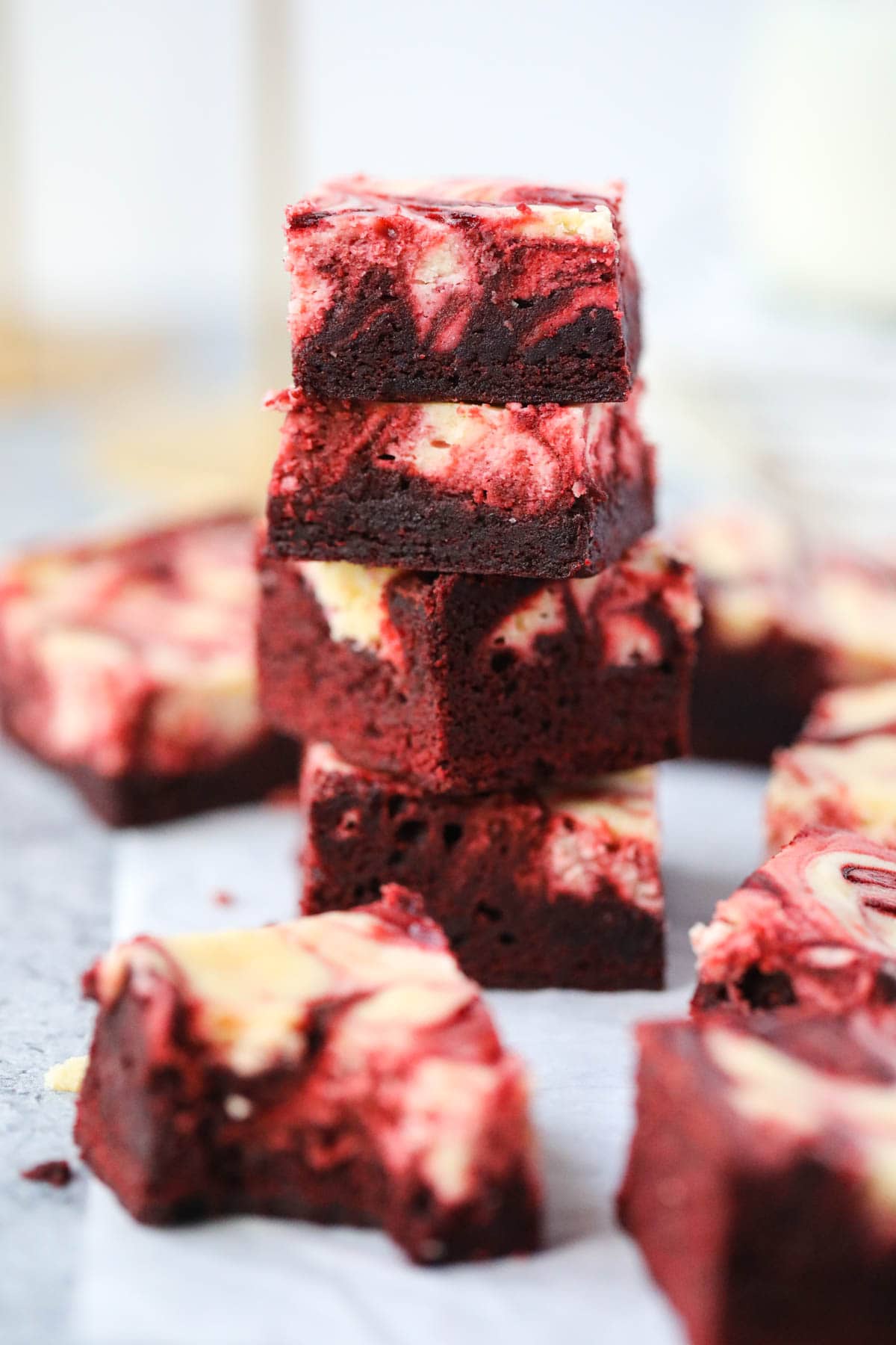 Red velvet cheesecake brownies stacked on parchment paper with a cup of milk in the background.