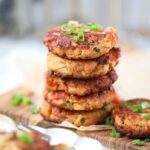 Southern salmon croquettes stacked on a wooden cutting board topped with sliced green onions.