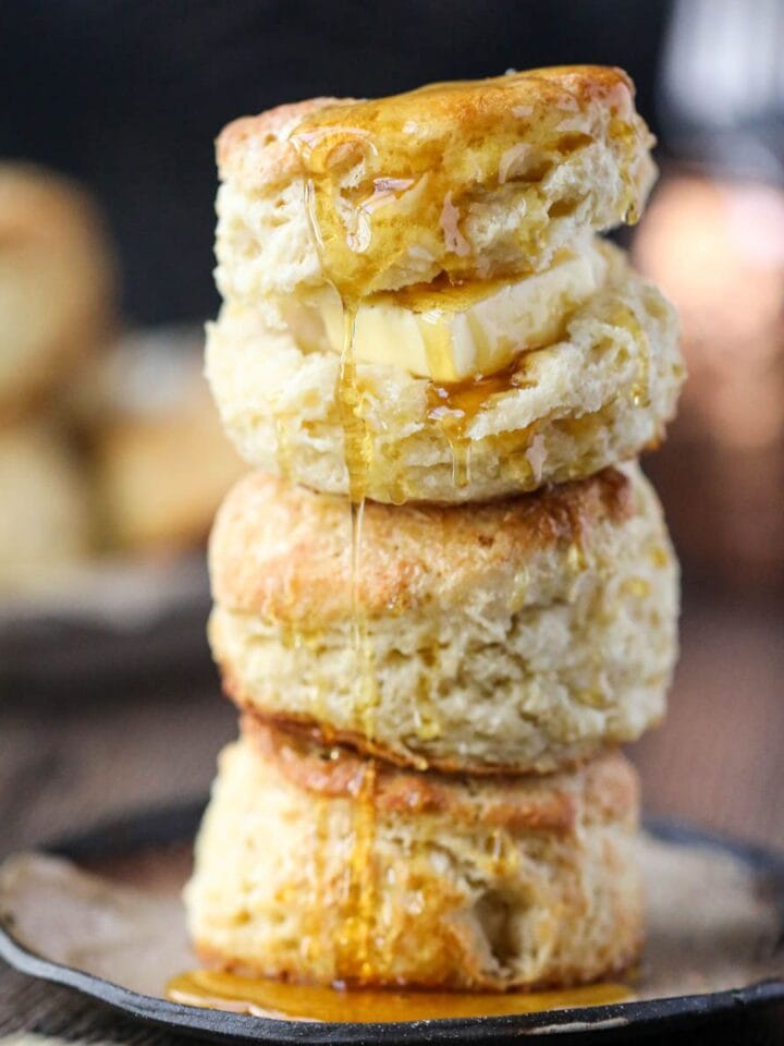 Southern buttermilk biscuits stacked on a plate with honey dripping over the top.