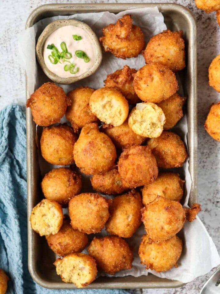 Southern hush puppies in a metal baking pan with a blue linen underneath on top of a white surface.