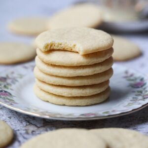 Old-fashioned southern tea cakes stacked on a white plate with a cup of hot tea in the background.