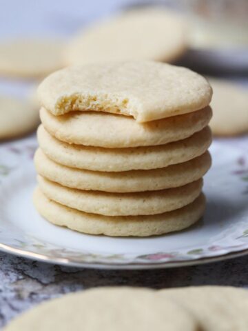 Old-fashioned southern tea cakes stacked on a white plate with a cup of hot tea in the background.