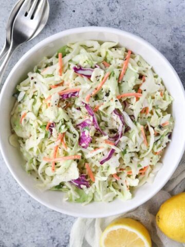 Southern coleslaw in a white bowl sitting on a white surface.