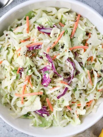 Southern coleslaw in a white bowl sitting on a white surface.