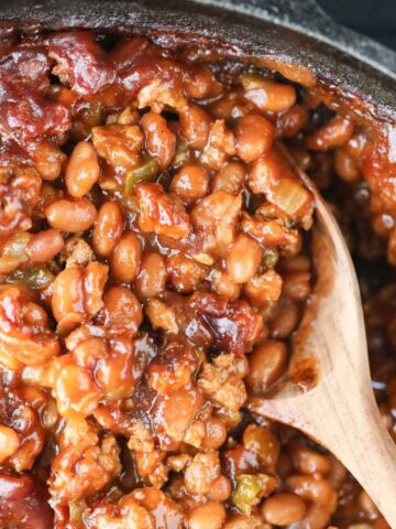 Southern baked beans in a cast iron skillet with a wooden spoon.