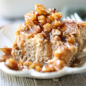 Serving of bread pudding with maple praline sauce on a white plate.