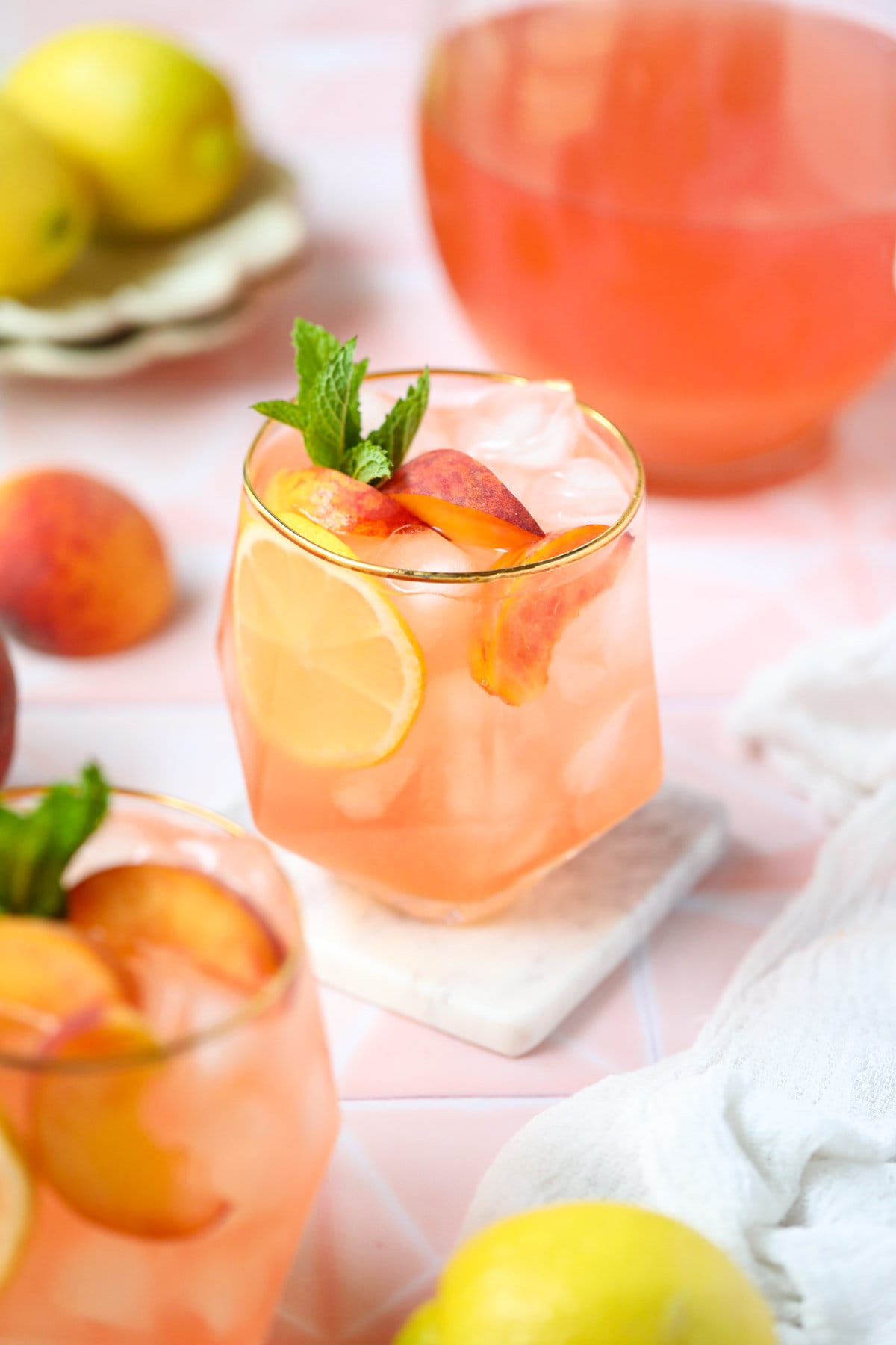 Fresh peach lemonade in a clear glass sitting on top of a pink surface.