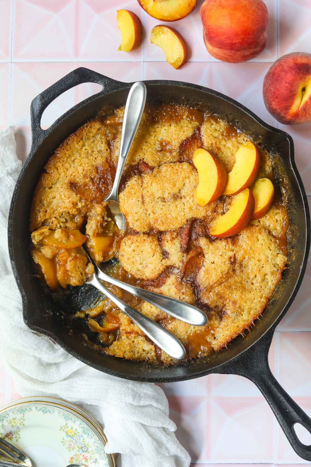 Skillet peach cobbler in a cast iron skillet sitting on top of a pink surface.
