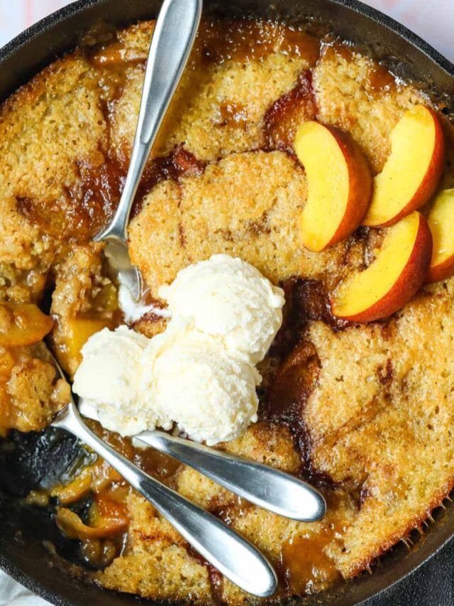 Skillet peach cobbler in a cast iron skillet sitting on top of a pink surface.