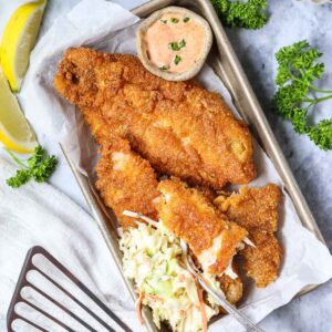 Southern fried catfish served with coleslaw on a serving tray sitting on top of a gray surface.