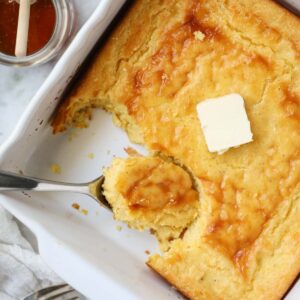 Southern spoon bread in a white baking dish sitting on top of a marble surface.