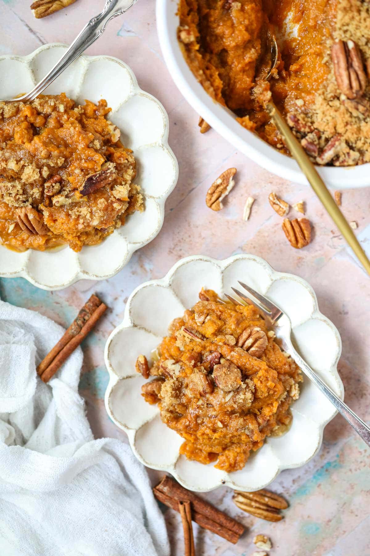 Servings of southern sweet potato casserole on white plates sitting on top of a tile surface.