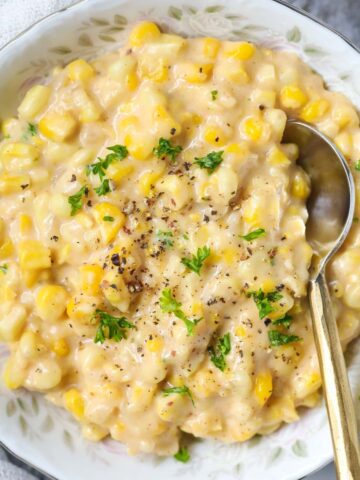 homemade creamed corn in a white bowl with a silver spoon.