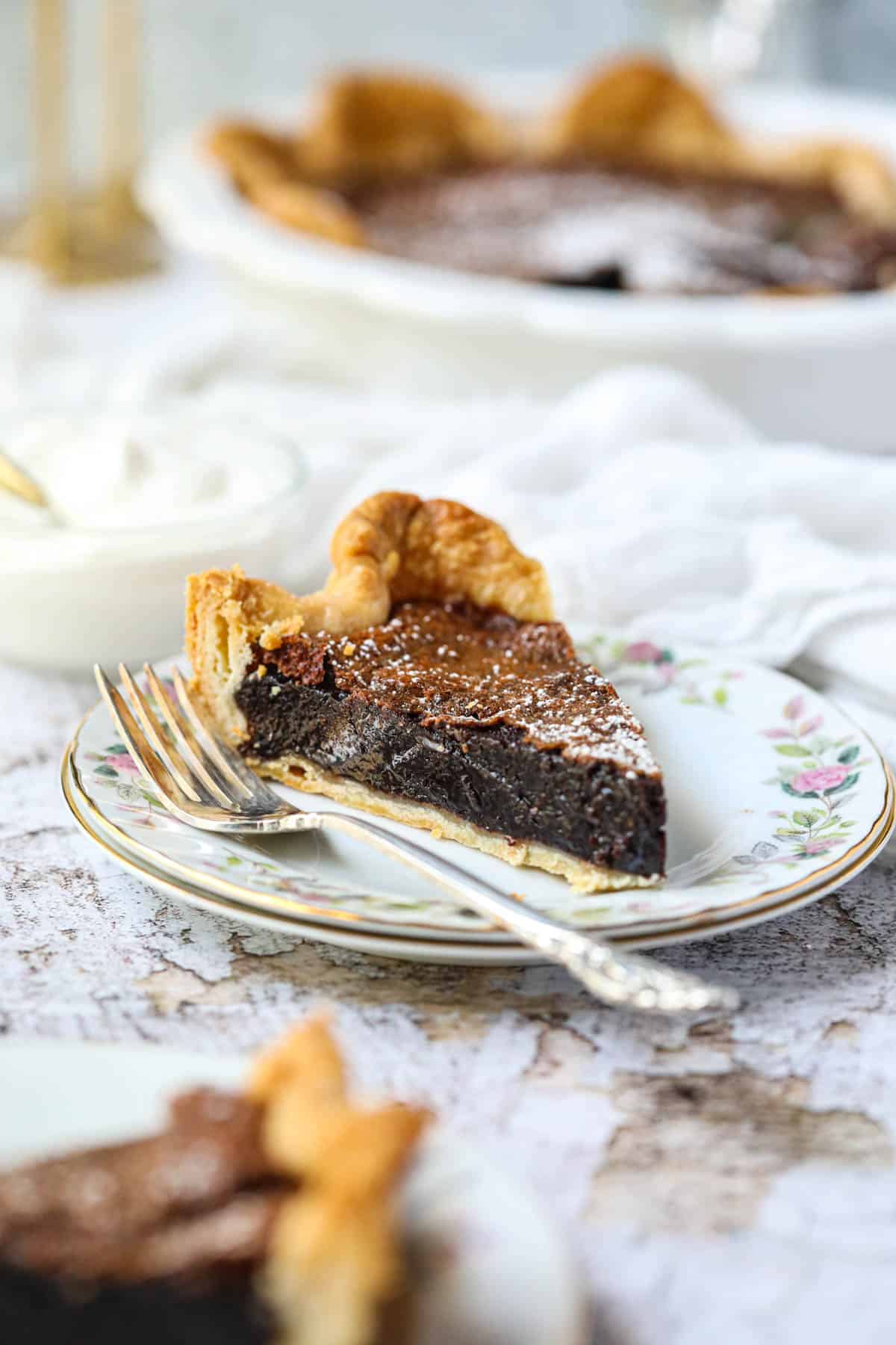 A slice of chocolate chess pie on a white dessert plate with a silver fork.