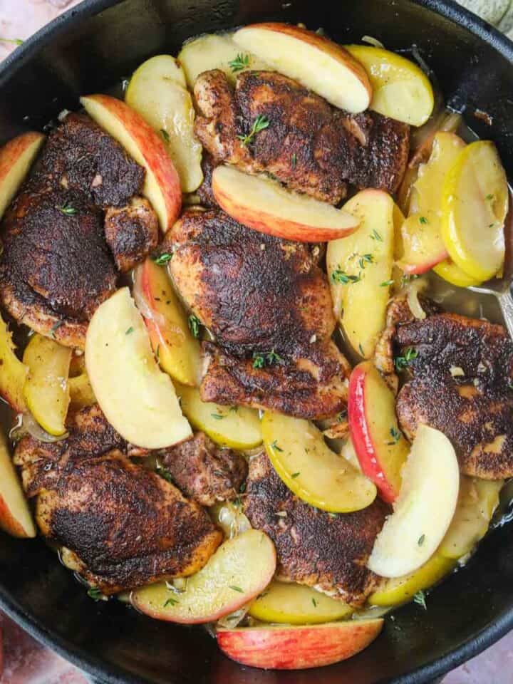 Apple cider chicken in a cast-iron skillet with a silver spoon.