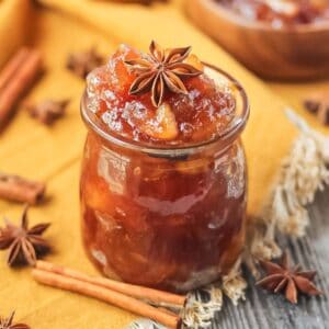 apple jam in a glass jar sitting on a wooden surface.