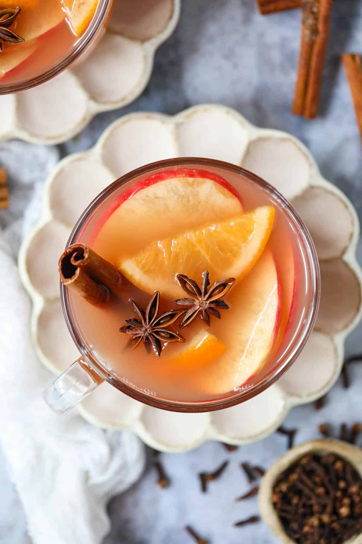 Homemade hot apple cider in a clear glass mug sitting on a gray marble surface.