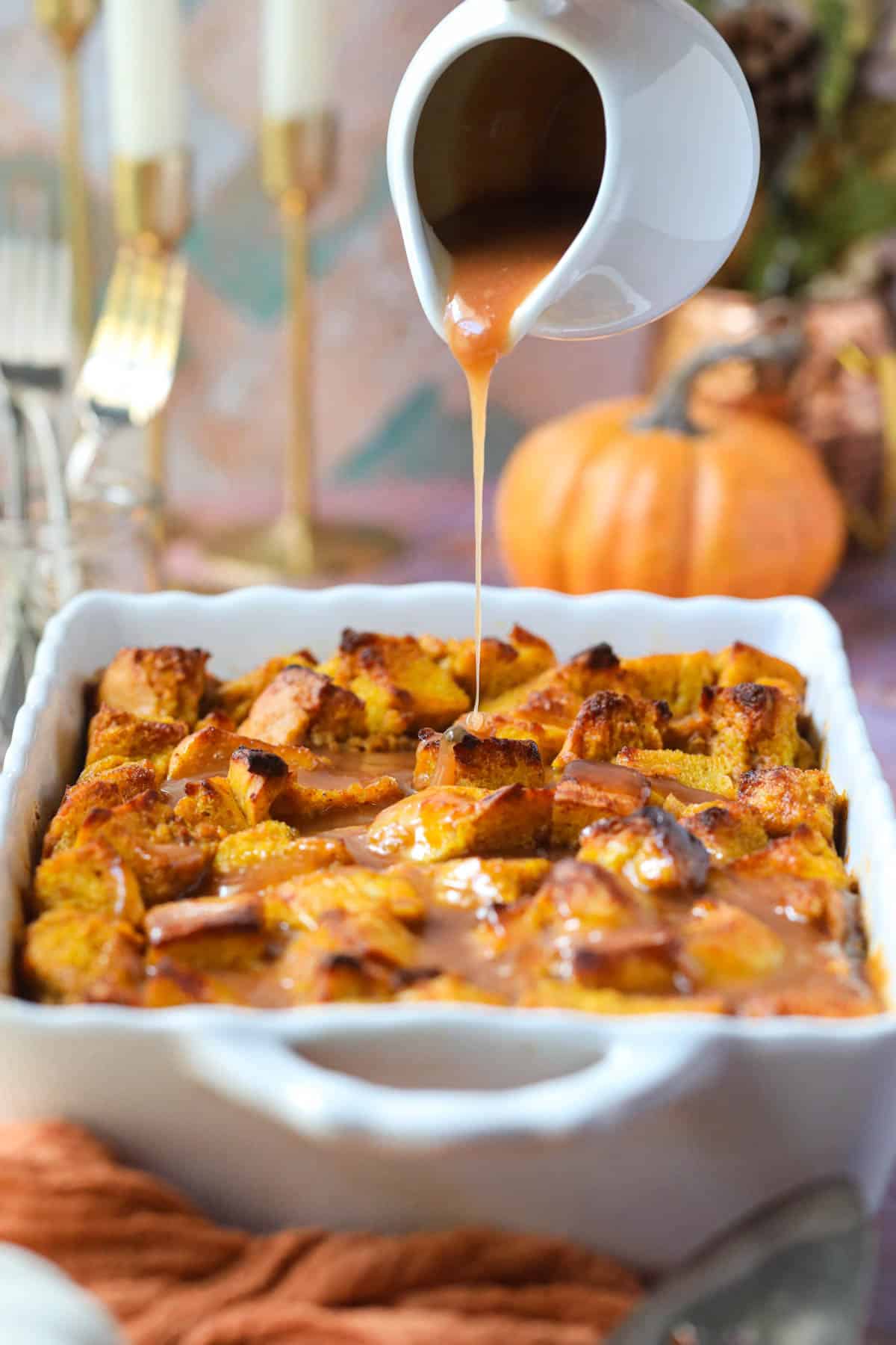 Pumpkin bread pudding in a white baking dish with salted caramel sauce being poured over top.