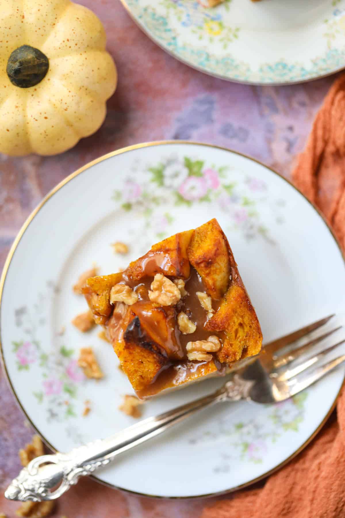 Pumpkin bread pudding with salted caramel sauce and chopped walnuts on a dessert plate with a silver fork.