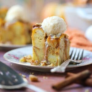 A serving of pumpkin bread pudding with salted caramel sauce and vanilla ice cream on a white dessert plate with a silver fork.