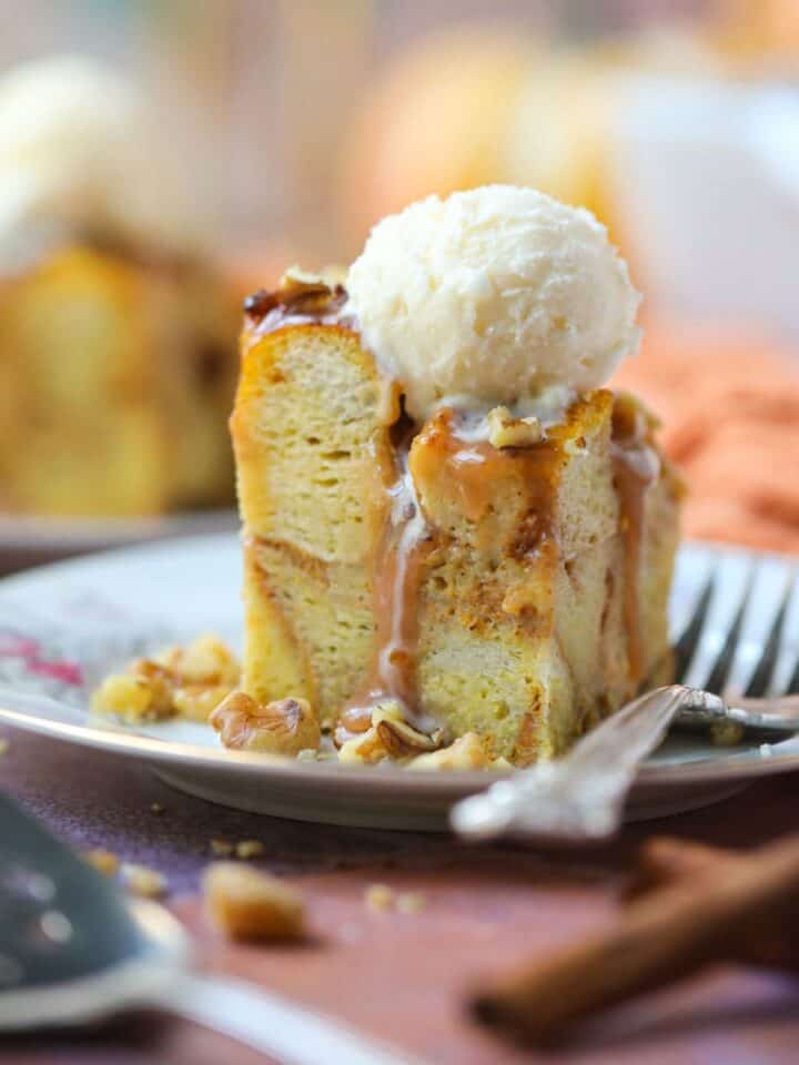A serving of pumpkin bread pudding with salted caramel sauce and vanilla ice cream on a white dessert plate with a silver fork.