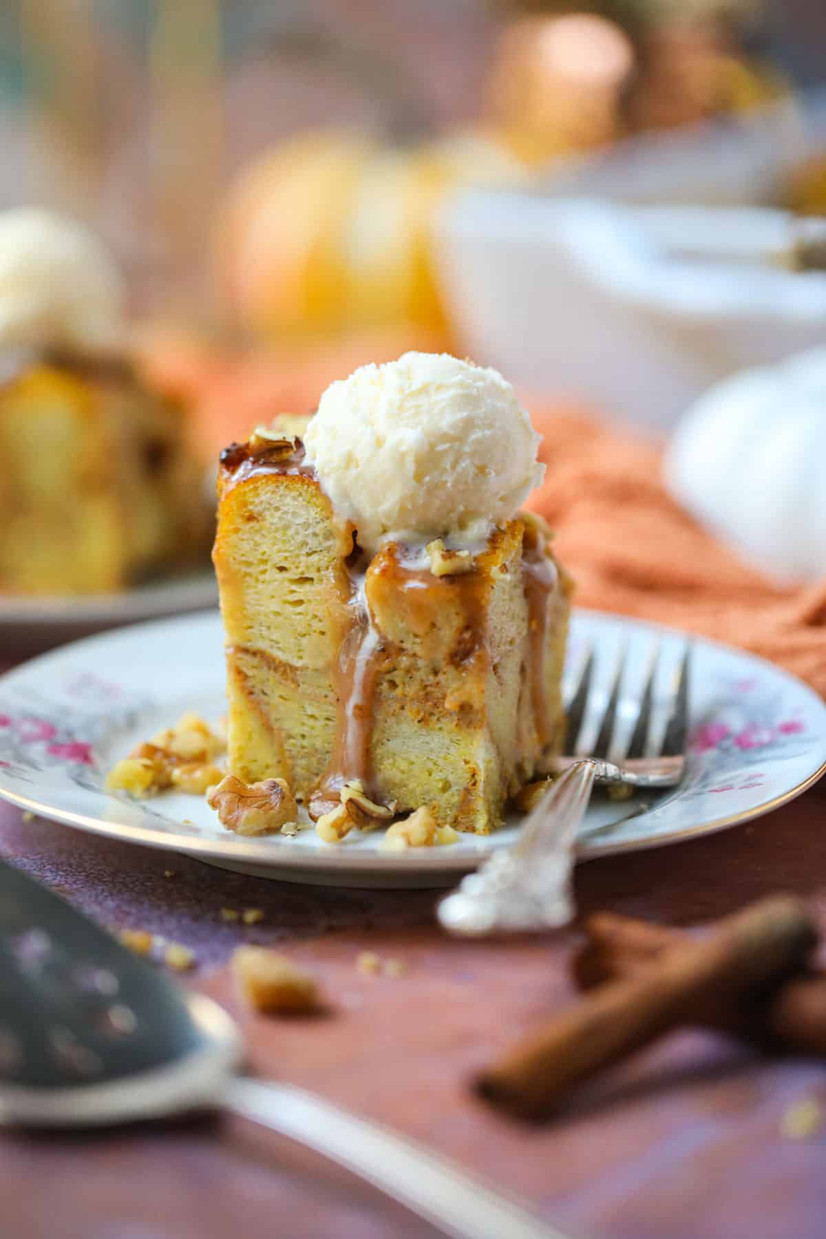 A serving of pumpkin bread pudding with salted caramel sauce and vanilla ice cream on a white dessert plate with a silver fork.