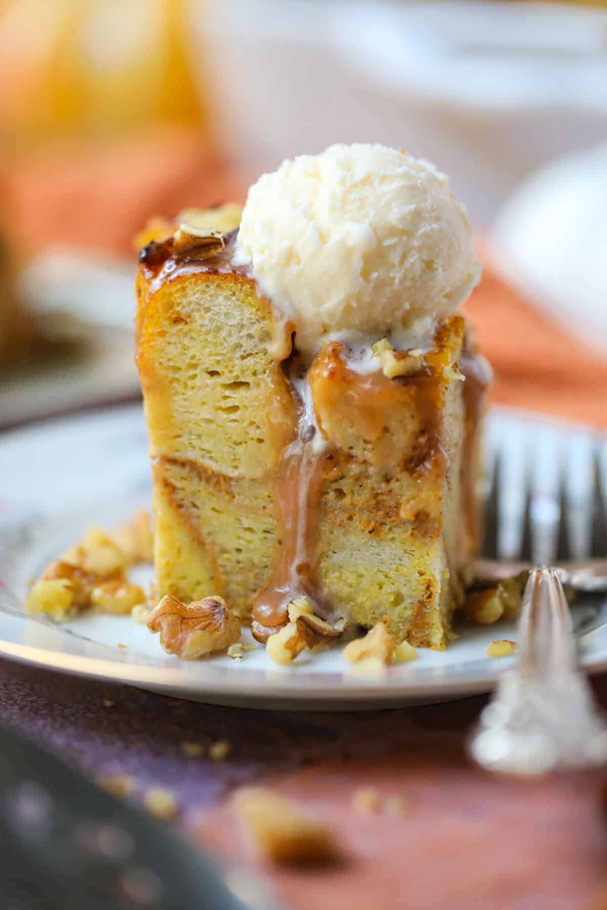 A serving of pumpkin bread pudding with salted caramel sauce and vanilla ice cream on a white dessert plate with a silver fork.