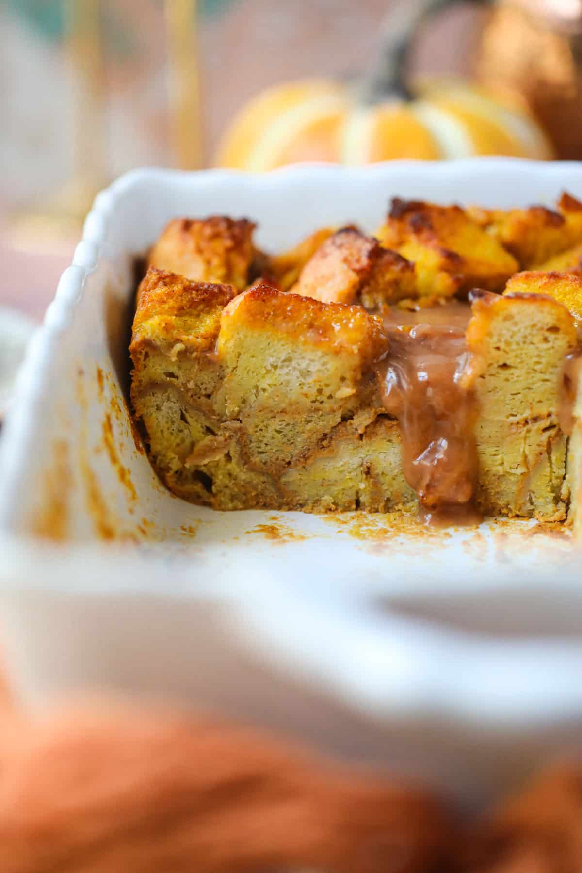 Pumpkin bread pudding with salted caramel sauce that has been sliced in a white baking dish.