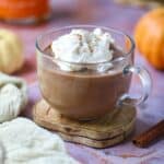 Pumpkin hot chocolate in a clear mug topped with whipped cream sitting on a copper tile surface.