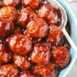 Cranberry meatballs in a blue serving bowl with a silver serving spoon.
