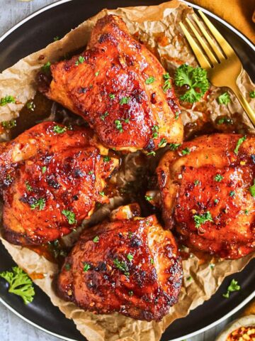 Hot honey chicken thighs on a black plate sitting on top of a white wooden surface.