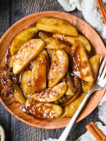 Southern fried apples on a wooden plate sitting on top of a wooden surface.