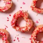 Baked strawberry donuts arranged on a table top.
