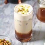 Iced pistachio latte in a tall glass sitting on a marble surface.