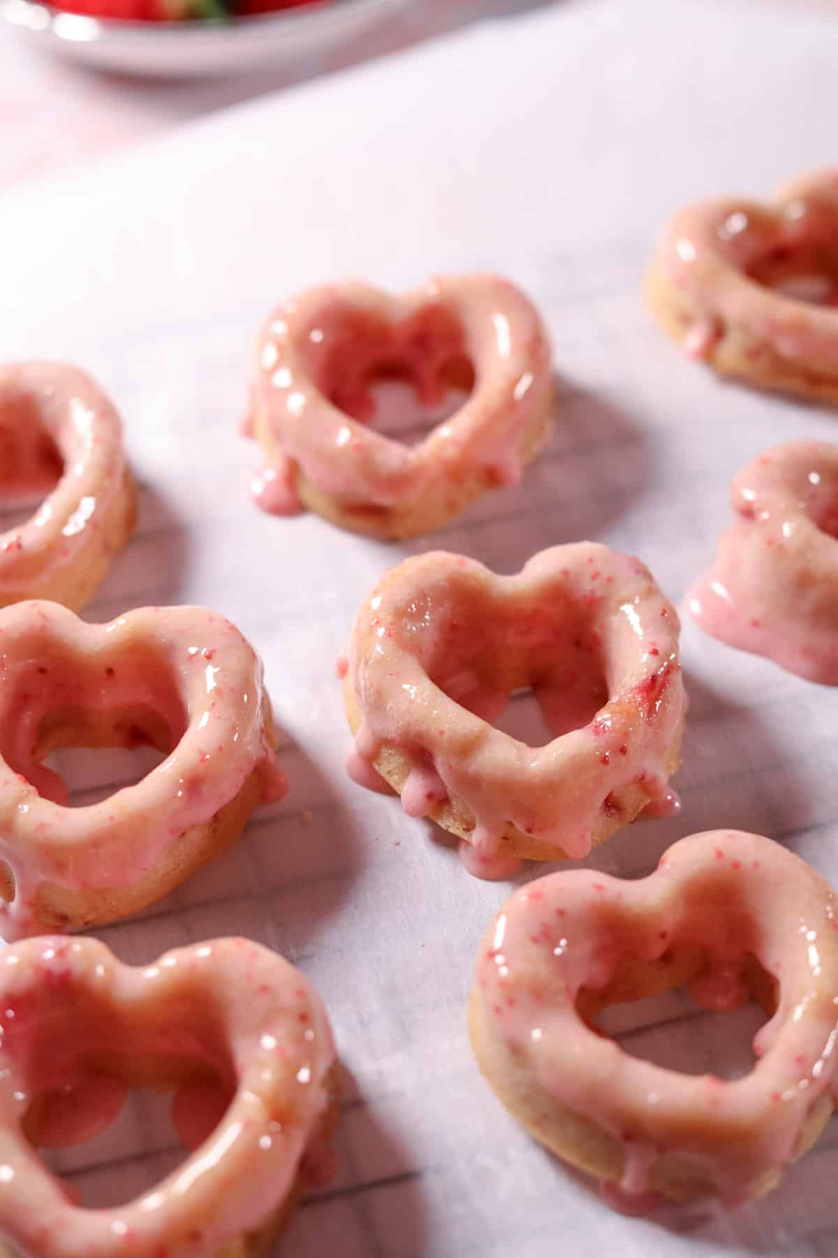 Glazed baked strawberry donuts arranged on parchment paper.