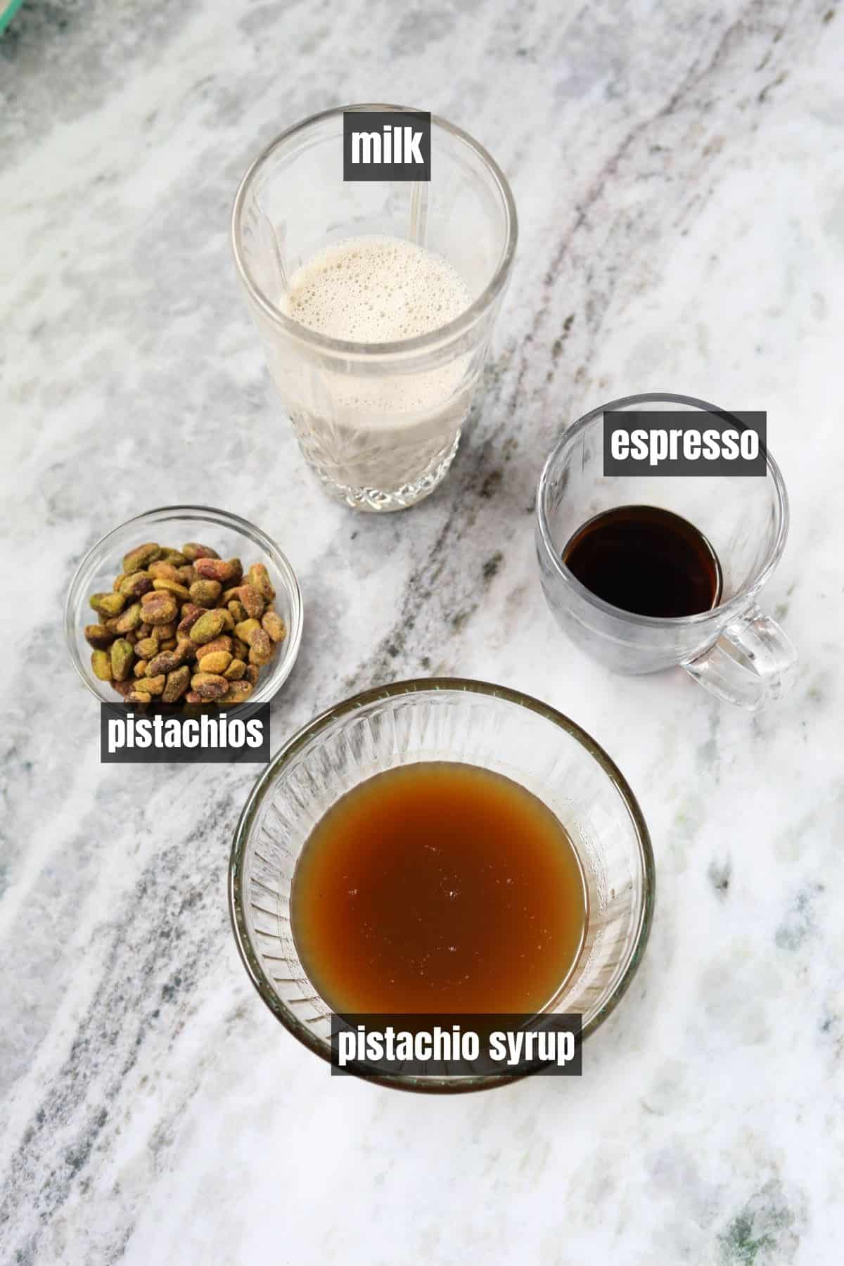 Ingredients for making an iced pistachio latte arranged on a marble table top.