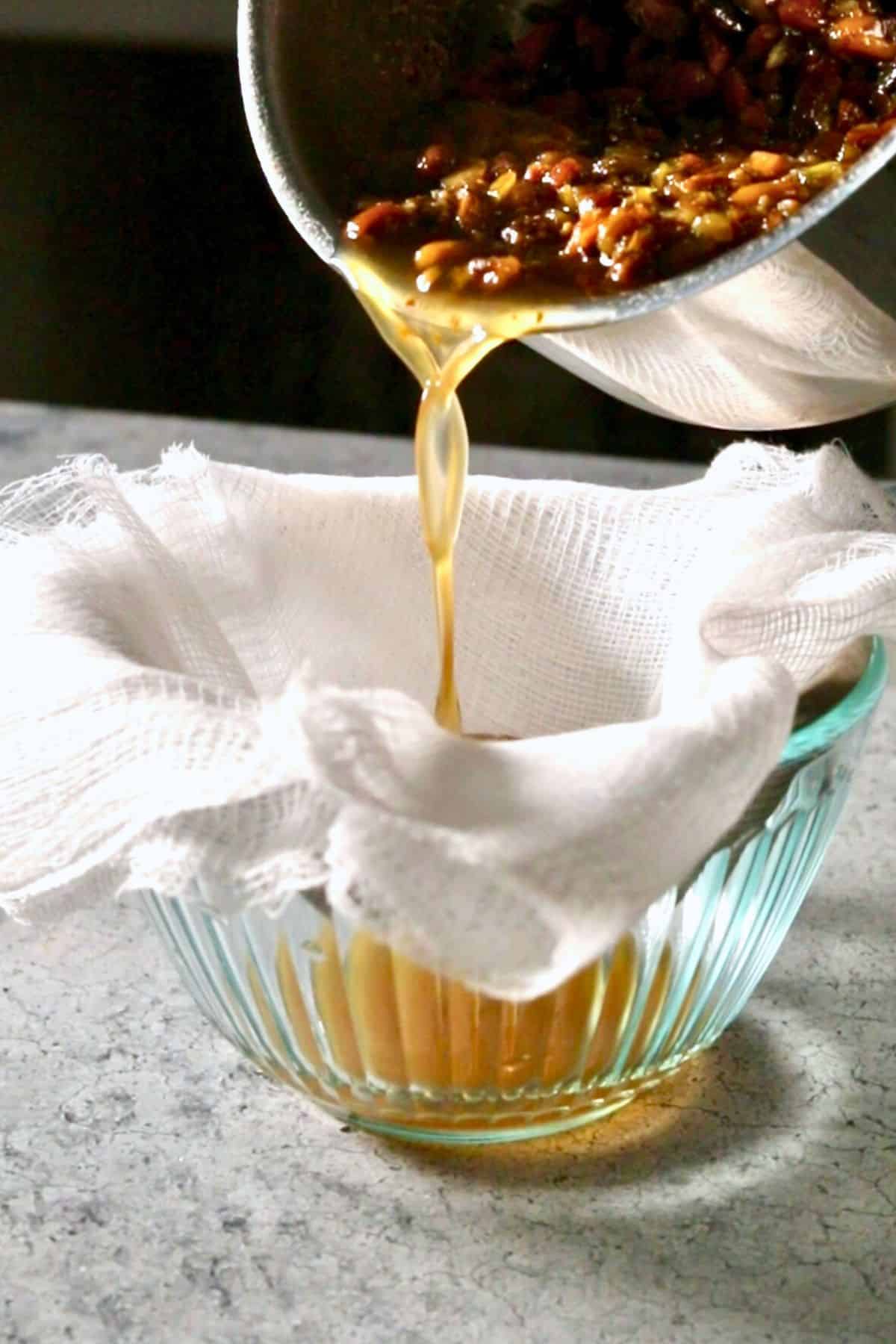 Straining pistachio syrup through a mesh sieve lined with cheesecloth.