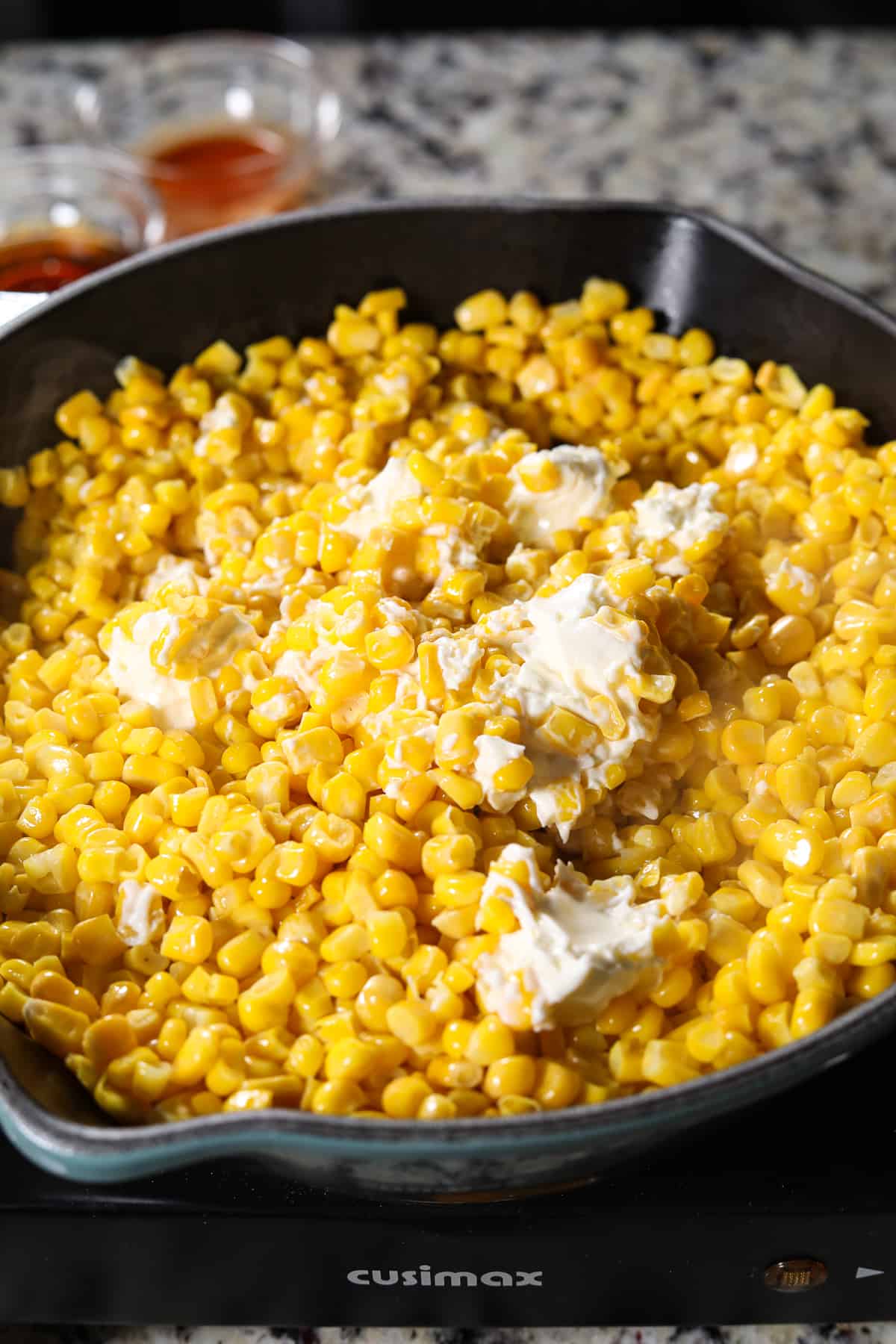 Corn cooking in a cast iron skillet with honey and cream cheese.