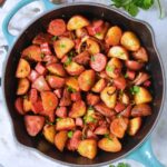 Skillet potatoes with smoked sausage in a cast iron skillet sitting on top of a marble table top.