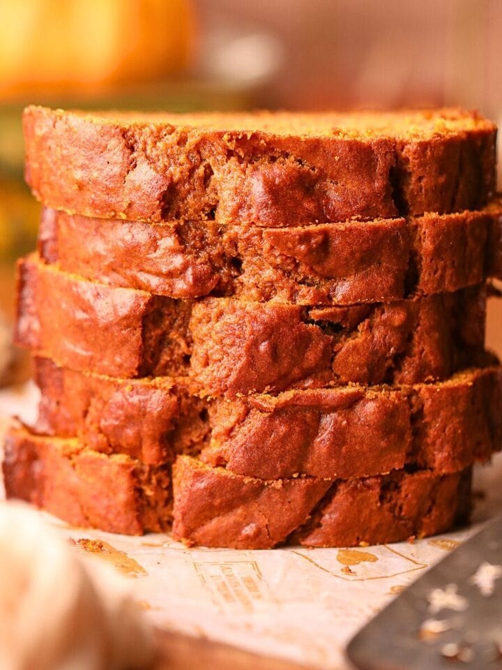 Slices of pumpkin banana bread stacked on a wooden cutting board.