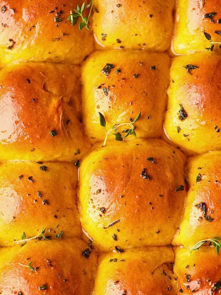 Soft herb pumpkin dinner rolls in a baking dish.