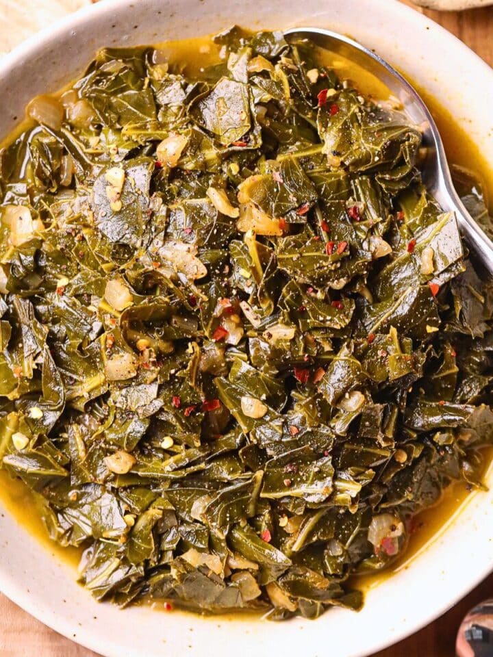 vegan southern collard greens in a white bowl sitting on a cutting board.