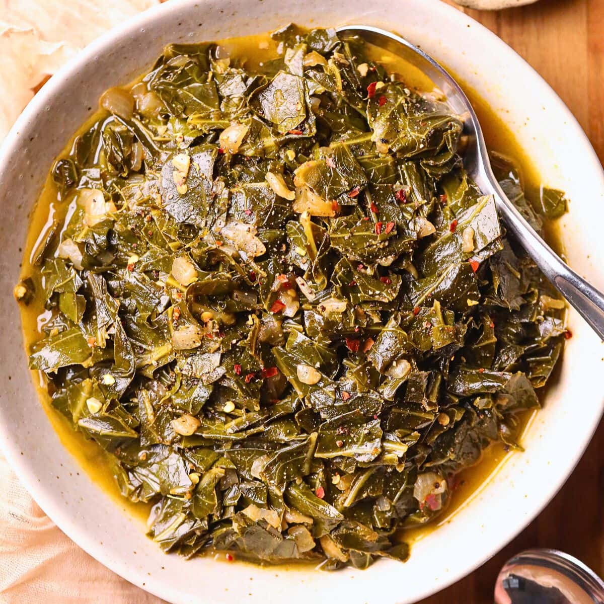 vegan southern collard greens in a white bowl sitting on a cutting board.